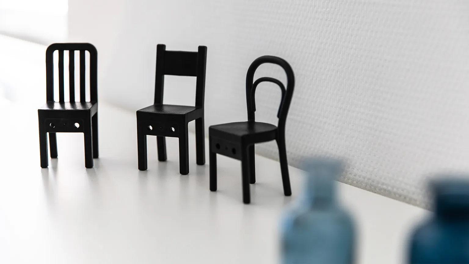 Drei Miniaturstühle stehen auf einem Regal.