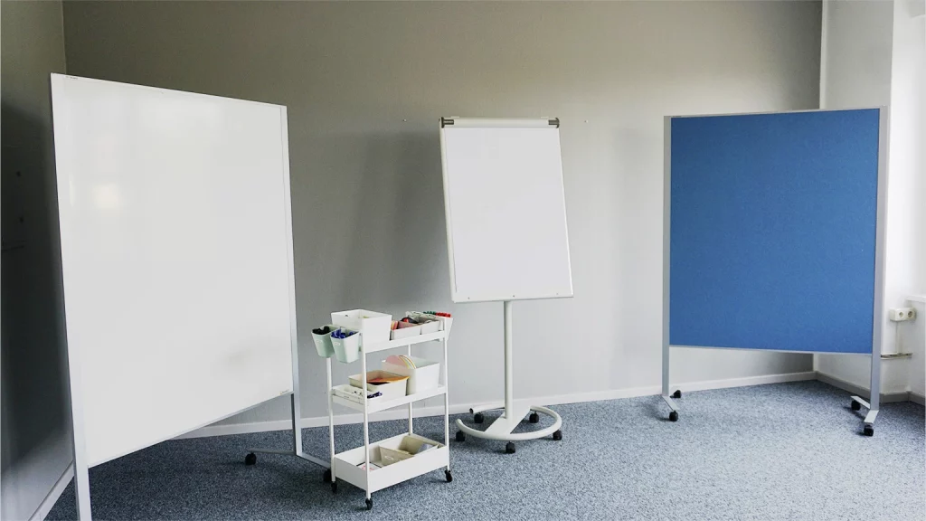 Seminarraum mit zwei Pinnwänden an den Seiten und einem Flipchart und Moderationswagen in der Mitte
