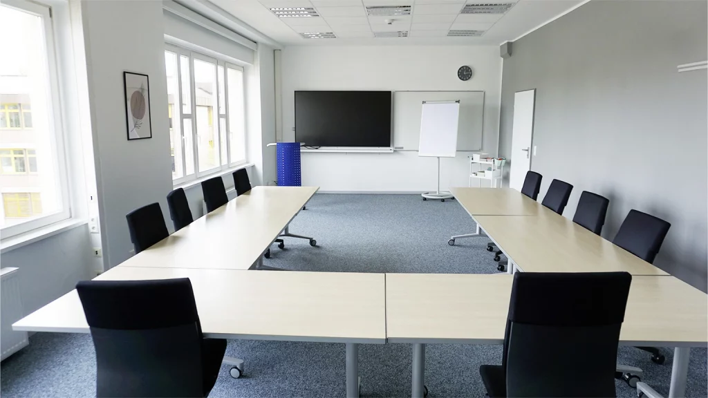Seminarraum in U-Form bestuhlt und Blick nach vorne auf Whiteboard, Bildschirm, Flipchart und Moderationswagen