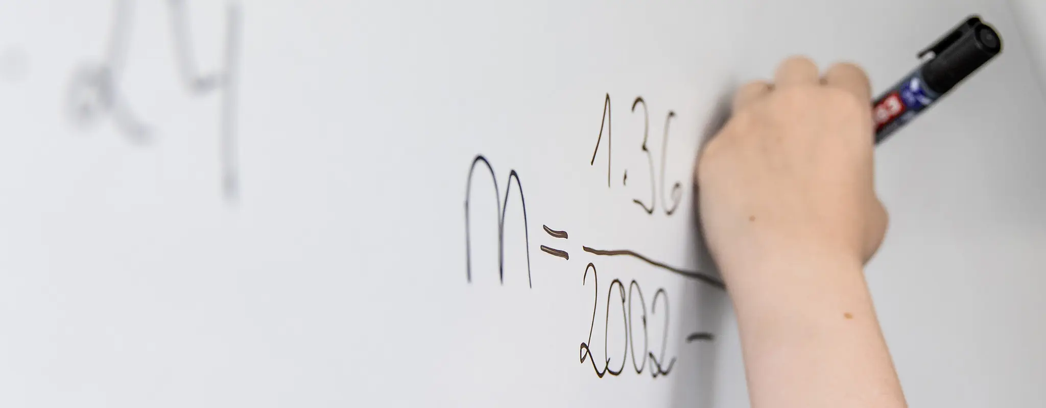 Person schreibt mit schwarzem Stift eine Formel an ein Whiteboard