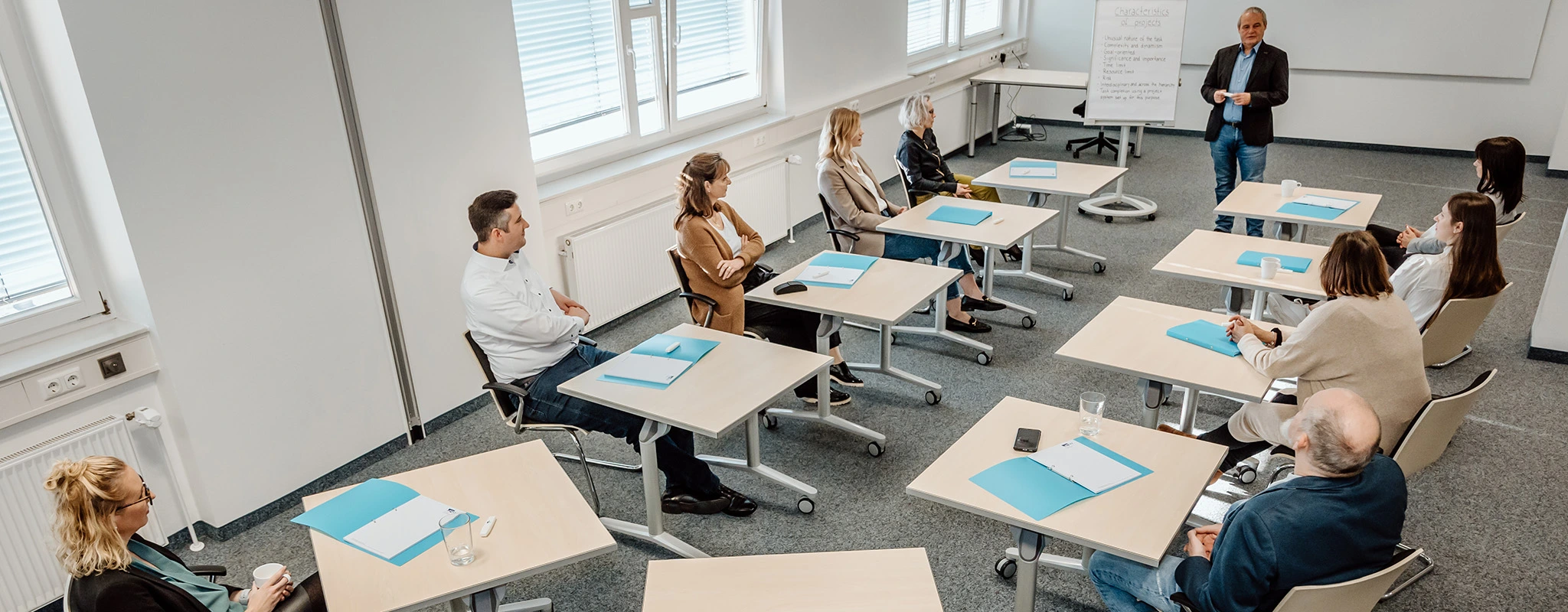 Seminarraum mit Einzeltischen und Personen, die zum Trainer schauen