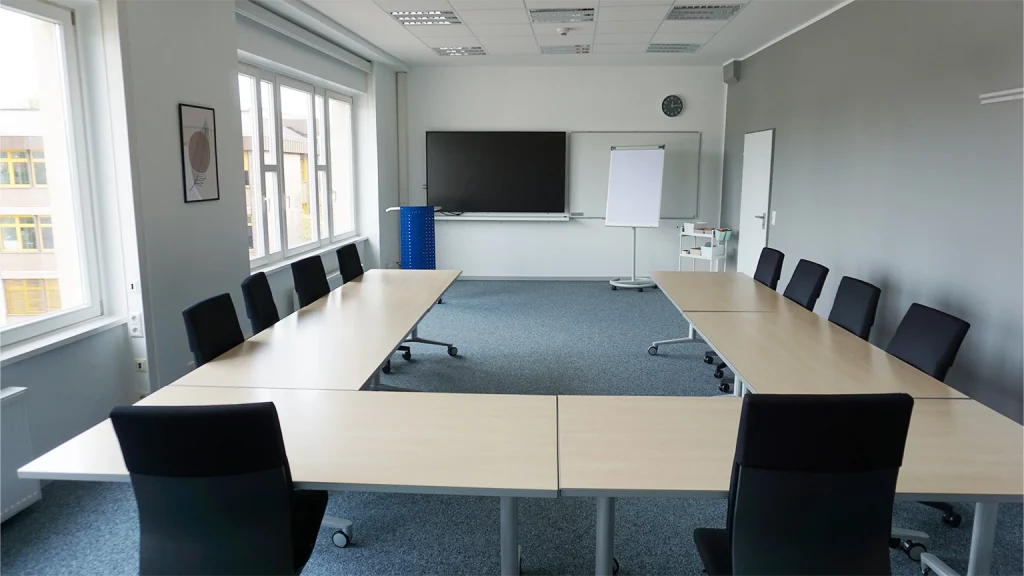 Seminarraum in U-Form bestuhlt und Blick nach vorne auf Whiteboard, Bildschirm, Flipchart und Moderationswagen