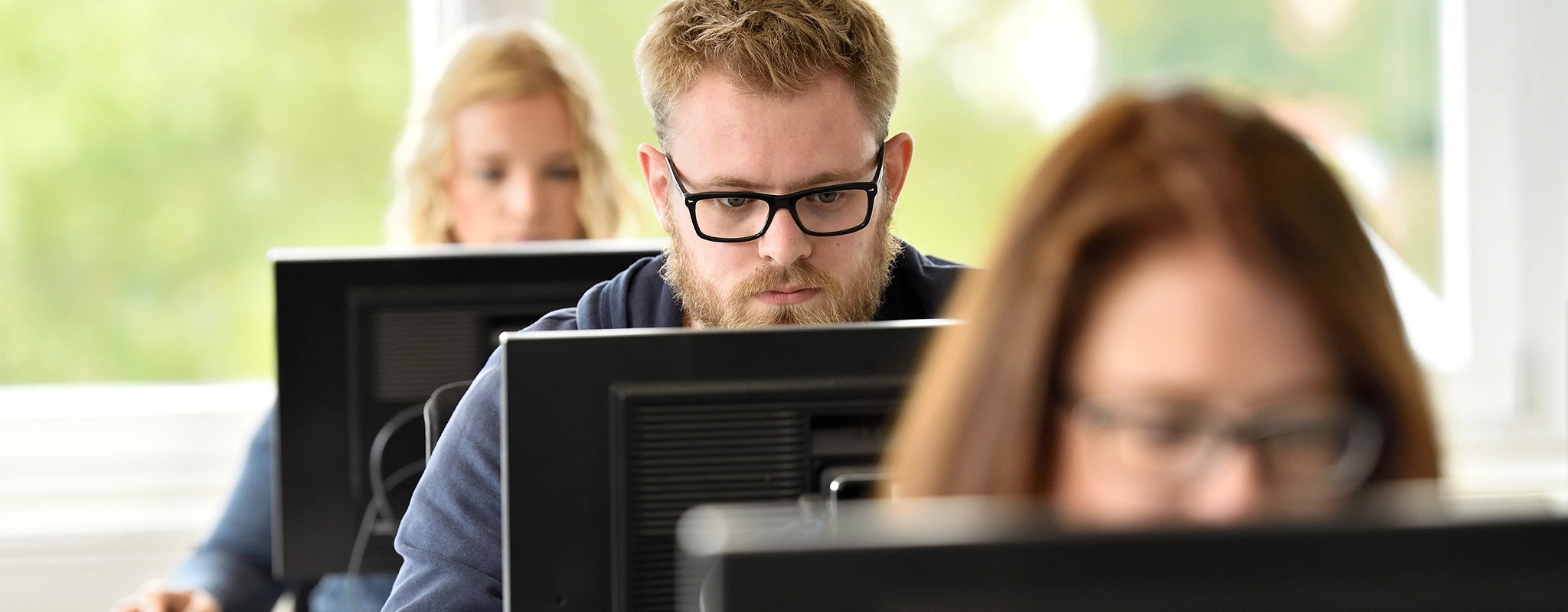 Drei Personen sitzen hintereinander ans Computern und schauen auf den Bildschirm