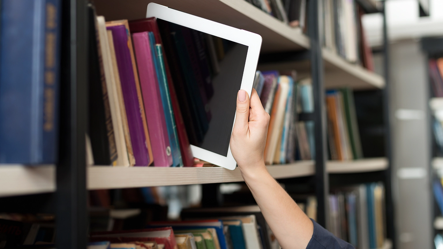 Hand nimmt Tablett aus einem Regal mit Buechern