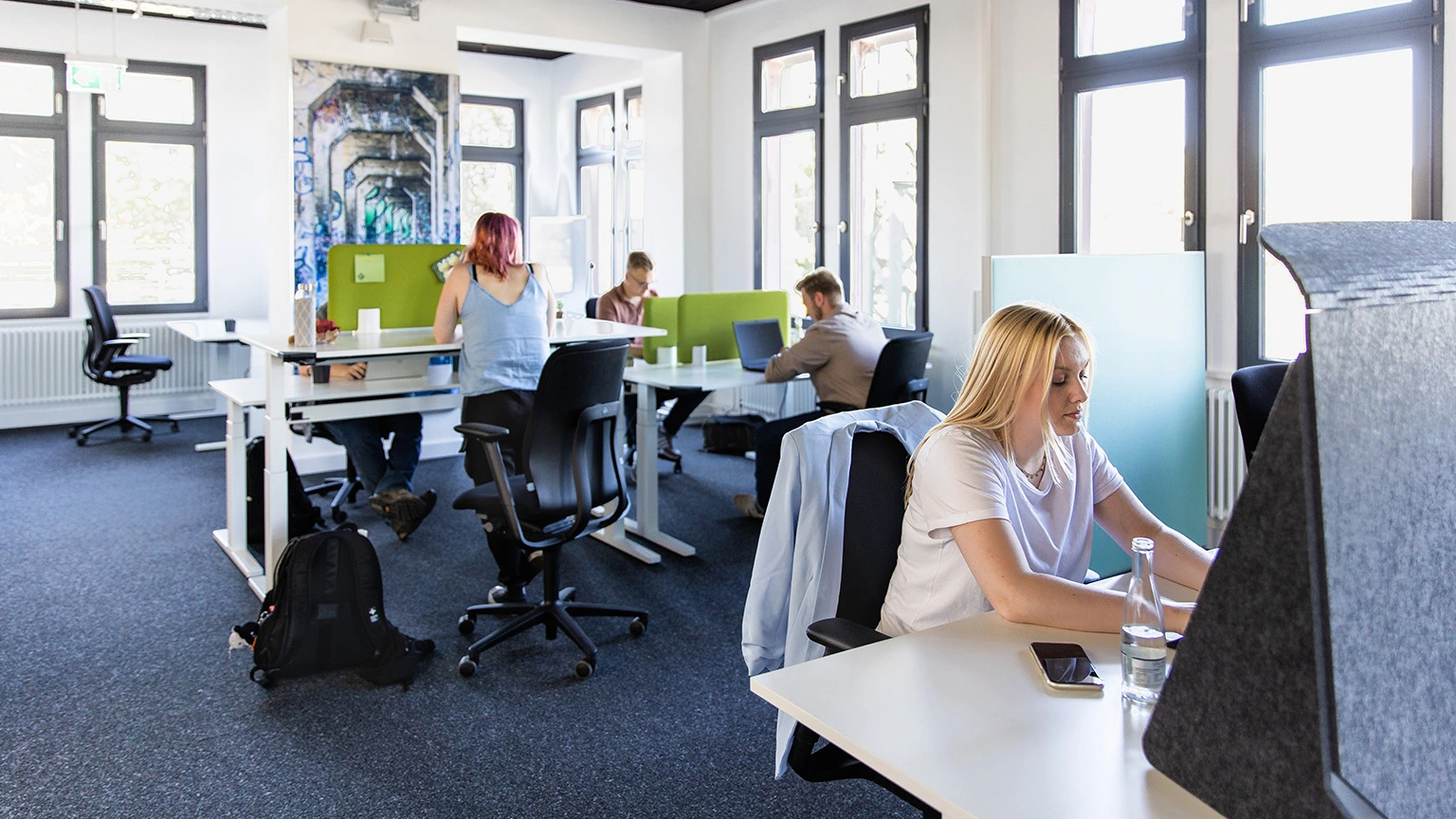 Personen an Schreibtischen vor Laptops in einem Coworking Space