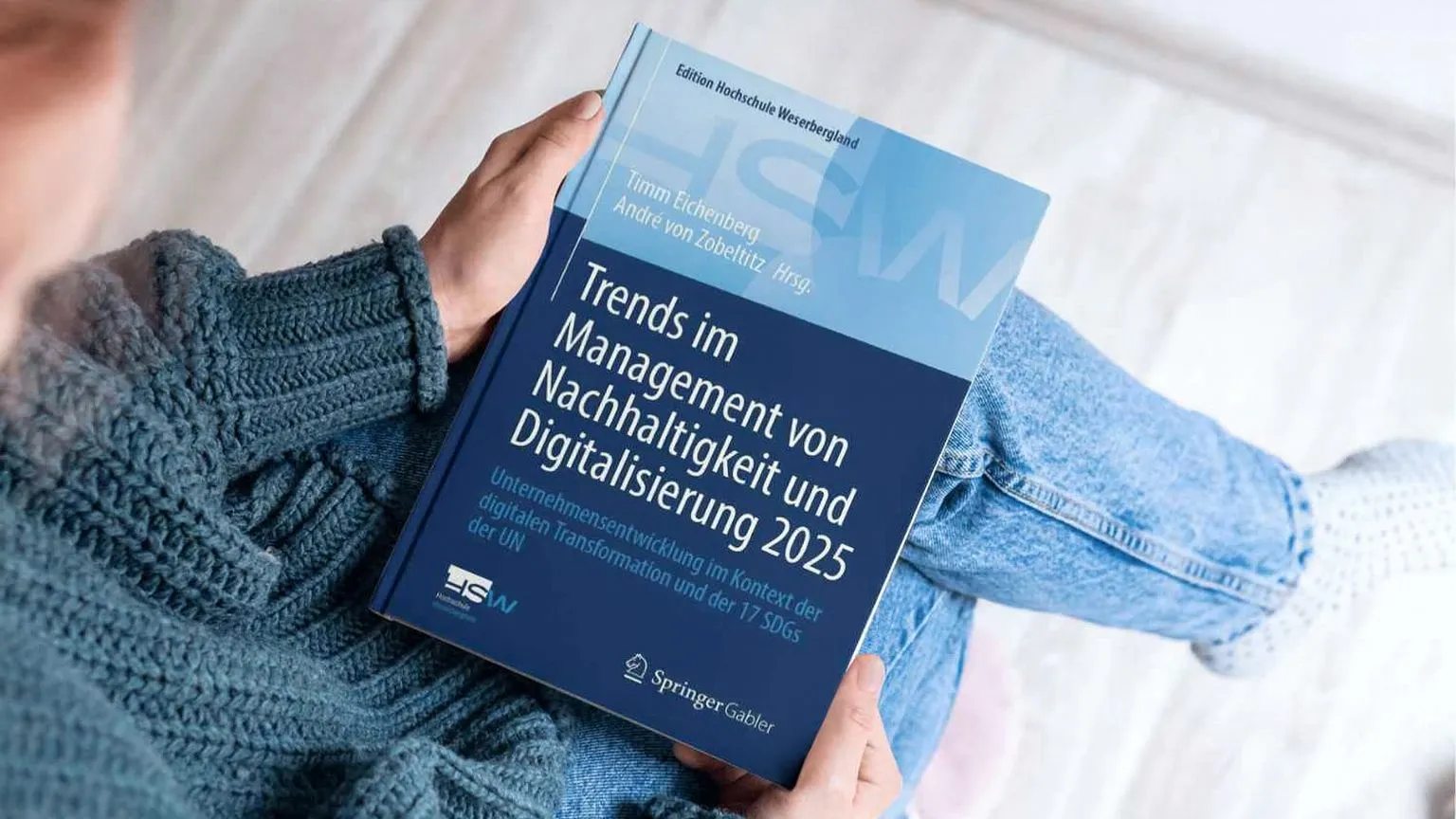 Eine Person hält das Buch Trends im Management von Nachhaltigkeit und Digitalisierung 2025 auf dem Schoß in den Händen